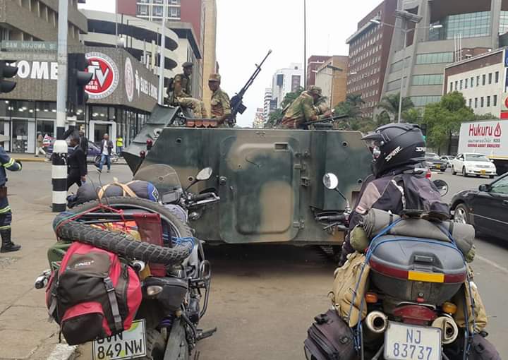 Military vehicles near 2 motorbikes